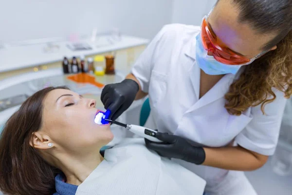 Paciente sentado en silla dental, doctor dentista usando equipo médico profesional — Foto de Stock