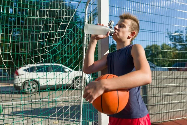 Fiú tizenéves kosárlabda játékos labda ivóvíz üvegből — Stock Fotó