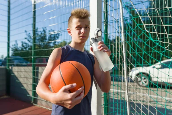 Chlapec teenager basketbalista s míčem pitné vody z láhve — Stock fotografie