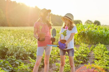 Portrait of two girls children with flowers in pots, gloves, with garden shovels
