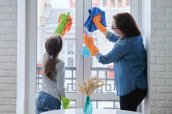 Mother and daughter child in gloves with detergent rag cleaning windows together — Stock Photo, Image