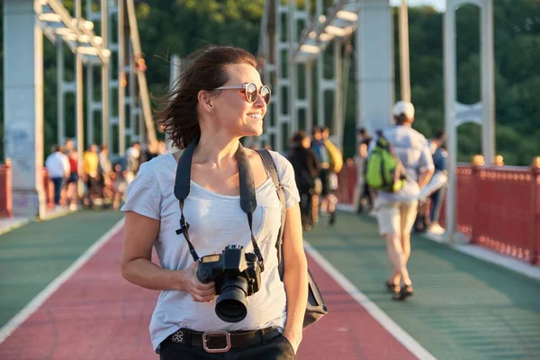 Volwassen vrouw met rugzak foto camera glimlachen op zonnige zomerdag — Stockfoto
