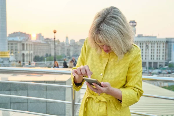 Зрелая женщина со смартфоном, пальцы на сенсорном экране, смс — стоковое фото