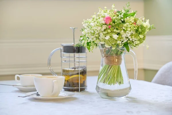 Table with white tablecloth tea in teapot, cups and bouquet of beautiful flowers — ストック写真