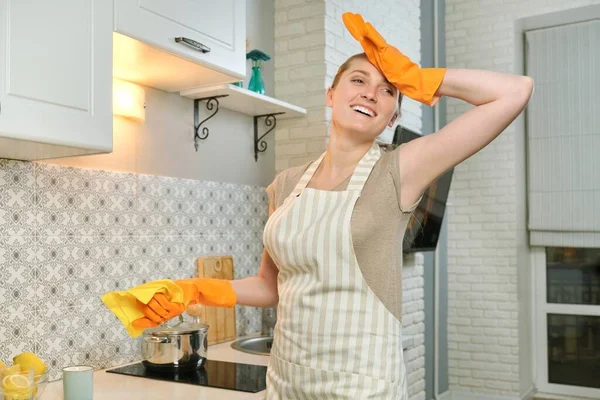 Tired woman in apron gloves doing house cleaning in the kitchen