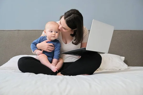 Молодая женщина с сыном малыша сидит в постели с ноутбуком — стоковое фото