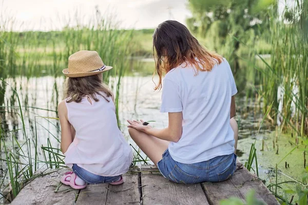 Barn vilar nära vattnet på sommardagen, leker med vattensniglar, bakifrån — Stockfoto