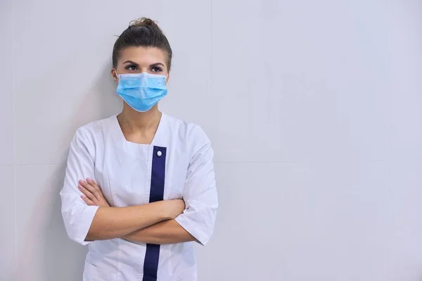 Молода серйозна впевнена жінка-лікар в медичній масці зі складеними руками — стокове фото