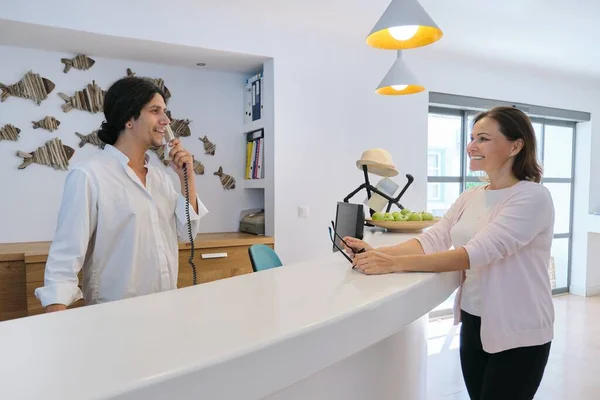 Resort hotel front desk, woman guest talking to man working at reception