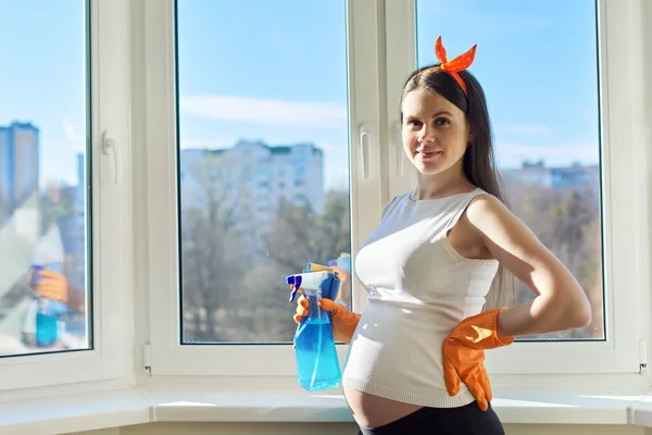 Pregnant woman in gloves looking at camera, near clean washed window — ストック写真