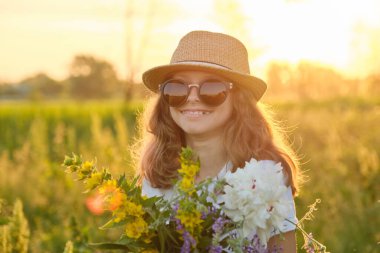 Portrait of child girl in hat sunglasses with flowers in meadow