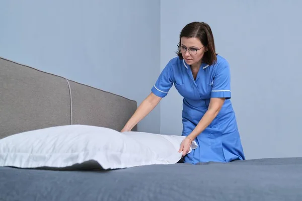 Cleaning service in hotel room, woman maid preparing guest room placing pillow