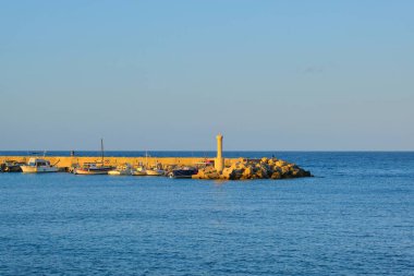 Küçük deniz feneri, rıhtımda yatlar, denizde gün batımı.