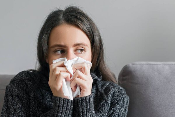 Sad sick young woman with handkerchief. Female with cough, snot, fever sitting at home on sofa, copy space