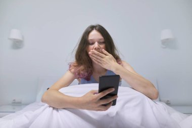 Evde oturup cep telefonuna bakan yorgun bir genç kız..