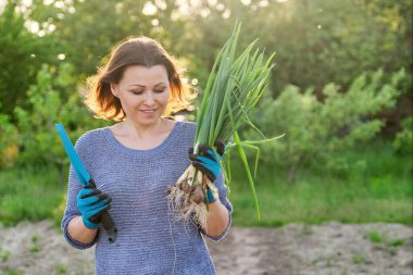 Taze yeşil soğan ile olgun kadın Açık bahar portre. Doğal organik sağlıklı gıda, arka plan sebze bahçesi, altın saat