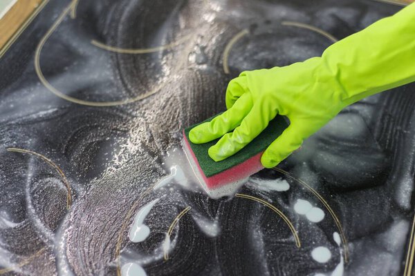 Closeup of hand woman cleaning modern cooking glass ceramic electric surface with sponge and detergent