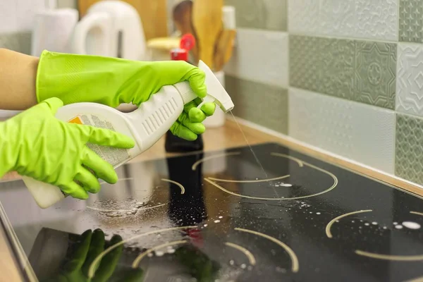 Woman hands in gloves cleans kitchen electric ceramic hob with sponge and detergent