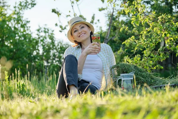 暑假在花园里 女园丁坐在刚刚修剪好的草地上 用新鲜的草本天然浆果饮料让女性休息 — 图库照片