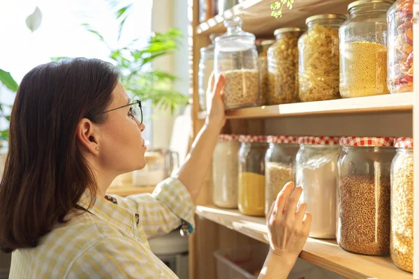 Food storage, wooden shelf in pantry with grain products in storage jars. Woman taking food for cooking