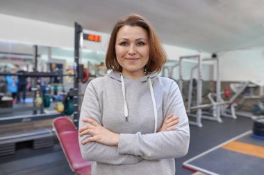 Spor salonunda elleri katlanmış orta yaşlı, kendine güvenen bir kadının portresi. Spor, spor, olgun insanların aktif sağlıklı yaşam tarzı.