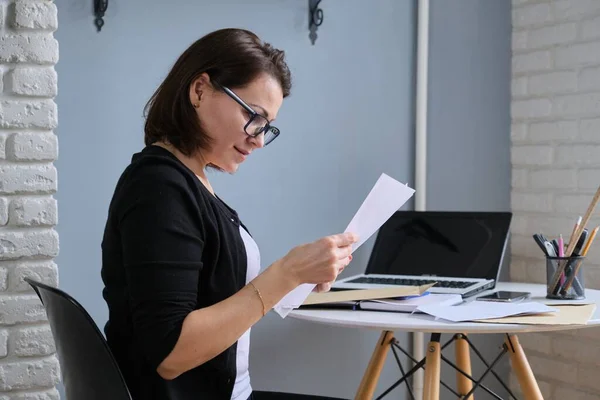 Dojrzała Kobieta Siedząca Przy Biurku Papierowym Dokumentem Uśmiechnięta Kobieta Czytająca — Zdjęcie stockowe