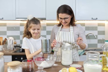 Anne ve çocuk ev mutfağında fırını birlikte hazırlıyorlar. Kadın un seçiyor, küçük kızına kek pişirmeyi öğretiyor. Ev yemeği, aile, ebeveyn çocuk iletişimi.