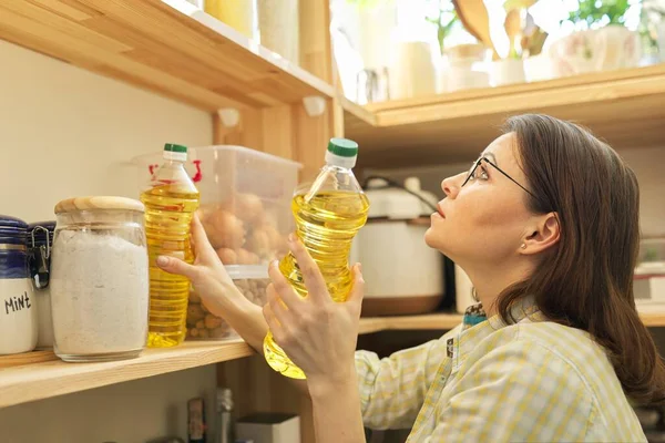 Food storage, wooden shelf in pantry with products. Woman taking food, sunflower oil for cooking.