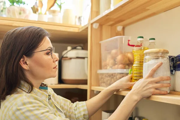 Food storage, wooden shelf in pantry with products. Woman taking food, sunflower oil for cooking.