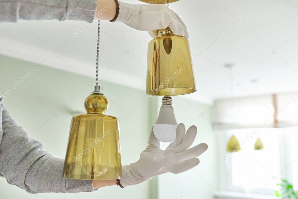 Hands installing LED bulb in lamp, chandelier.