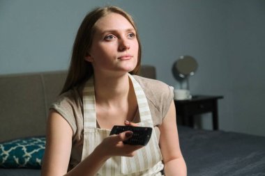 Uzaktan kumandalı güzel bir kadın, ciddi bir kadın evde oturuyor ve televizyon seyrediyor..