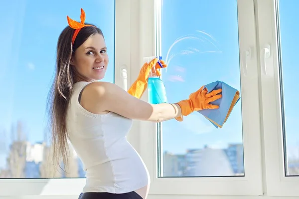 Молодая беременная женщина в перчатках с тряпкой моющего средства делает уборку дома — стоковое фото