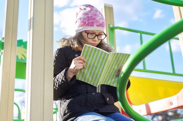 Smart child girl, 8-9 years old, in jacket hat glasses, reading book — Stock Photo, Image