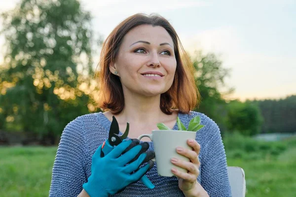Красива зріла жінка садівник в рукавичках з секаторами з чашкою трав'яного чаю — стокове фото