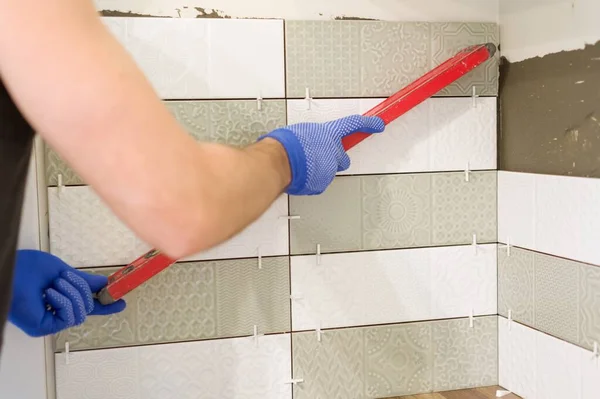 El trabajador masculino pega baldosas en la pared de la cocina, utiliza materiales y herramientas de nivel y profesionales —  Fotos de Stock