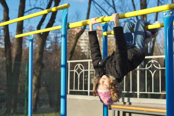 Girl child hanging upside down on outdoor sports playground with eyes closed — Stock Photo, Image