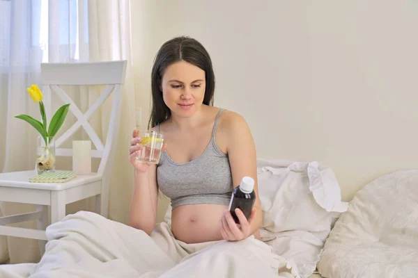 Těhotná žena čtení etikety na lahvičce s léky, s vitamíny — Stock fotografie