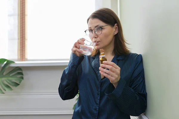 熟女は水のガラスで滴下,鎮静薬を飲みます,パジャマで自宅で — ストック写真