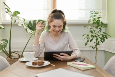 Genç kız evde oturmuş, ders çalışıyor, okuyor, dijital tablet kullanıyor.