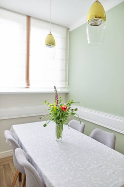 Parlak yemek odası, pencere kenarındaki masa ve sandalyeler, vazoda bir buket çiçek.