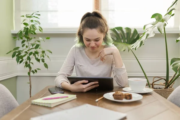 Дівчина-підліток сидить вдома за столом навчається, читає, використовує цифровий планшет для навчання — стокове фото