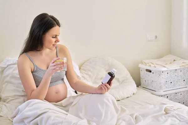Těhotná žena čtení etikety na lahvičce s léky, s vitamíny — Stock fotografie