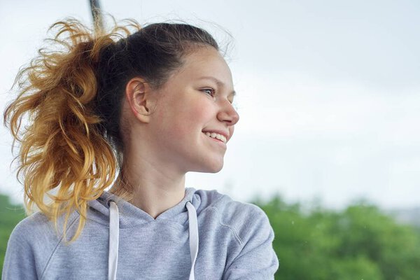 Closeup portrait of teenage girl of 14, 15 years old in gray sweatshirt. Background blue sky in clouds, copy space, place for text, back to school