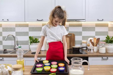 Mutfaktaki önlüklü kız, bir tepsi çiğ silikon kek hazırlıyor. Ev yemeği, ev yemeği, çocuklarla yemek pişirmek.