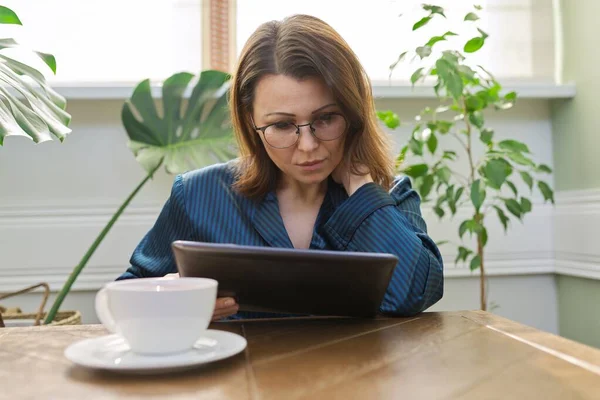 自宅読書メール ニュース デジタルタブレット上のソーシャルネットワークで成熟した深刻な女性 朝の女性のパジャマでお茶を飲んで — ストック写真