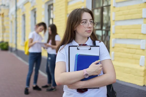 メガネの肖像画の女の子の学生10代のバックパックと白いTシャツを結ぶ 背景黄色のレンガ造りの建物 学生のグループ — ストック写真