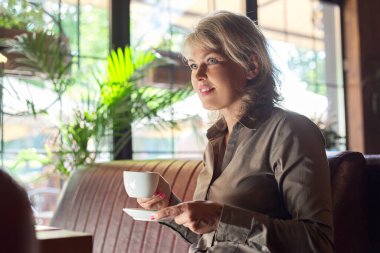 Lokantada kahve içen olgun, güzel bir kadın. İş kadını molada dinleniyor, boşluğu kopyala