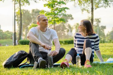 Orta yaşlı çift yoga minderinde oturuyor, kadın ve erkek rahatlatıcı içme suyu hakkında konuşuyorlar. Aktif sağlıklı yaşam tarzı, ilişki, spor, olgun insanlarda spor