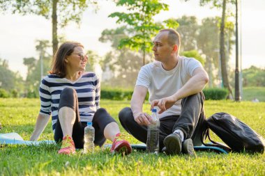 Orta yaşlı çift yoga minderinde oturuyor, kadın ve erkek rahatlatıcı içme suyu hakkında konuşuyorlar. Aktif sağlıklı yaşam tarzı, ilişki, spor, olgun insanlarda spor