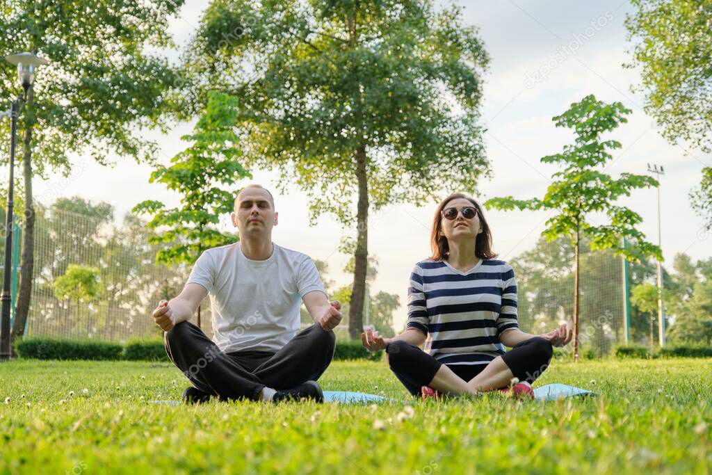 Couple, man and woman sitting in park on mat in lotus position and meditating. Yoga, fitness, active healthy lifestyle in middle-aged people